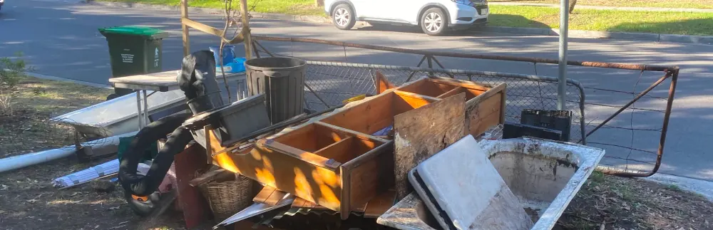 Old cabinets, a bathtub, a table and other household hard rubbish stacked on a nature strip