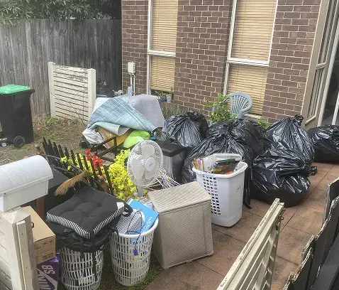 Bagged rubbish, laundry baskets, a fan and household items piled beside a brick unit, ready to be removed