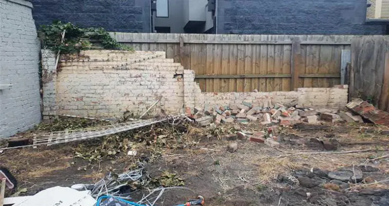 Before: a backyard covered in broken bricks, rubble and garden debris in front of a timber fence