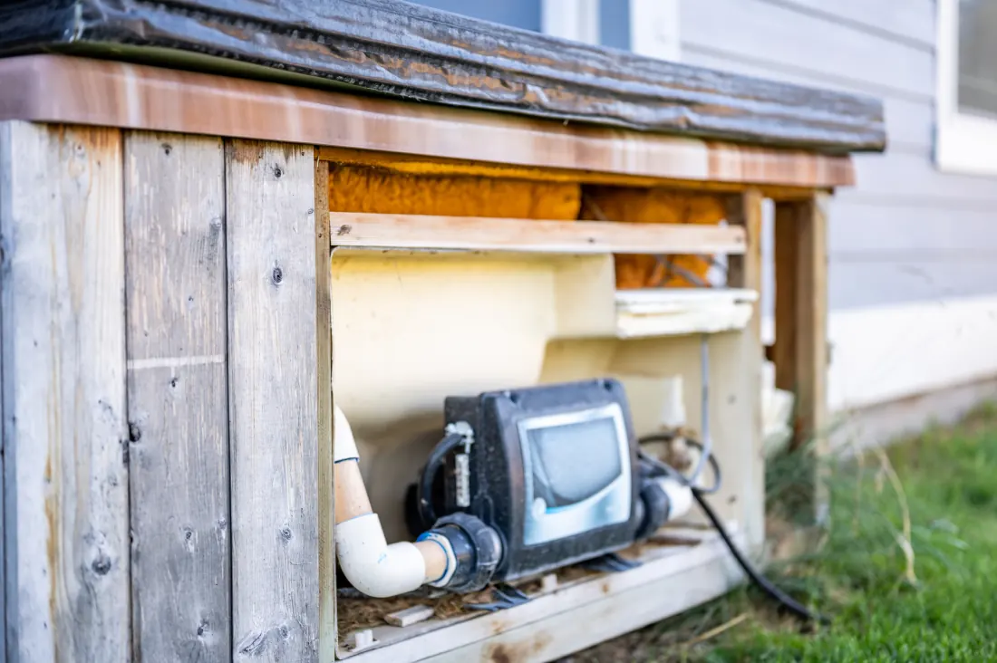 An old timber-clad outdoor spa with its pump equipment exposed