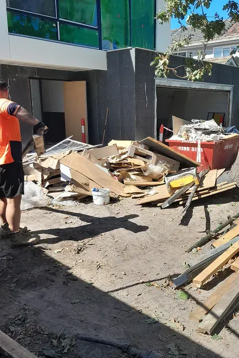 Timber offcuts and renovation waste piled at a building site, with a worker in high-vis nearby